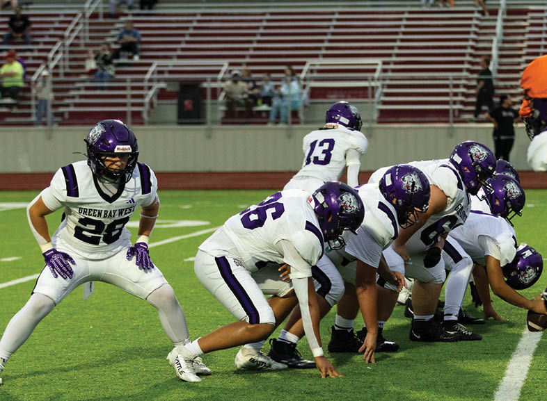 Four people wearing black football uniforms with “VISTA" on the front are standing together in a stadium with a crowd in the background, two of them holding helmets raised above their heads. Description generated by AI
