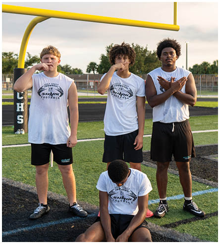 Three boys are standing on a football field. Description generated by AI