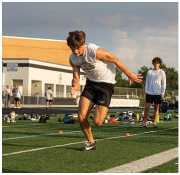 A man running on a field with a white shirt and black shorts. Description generated by AI