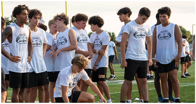 A group of young men are standing on a football field. Description generated by AI