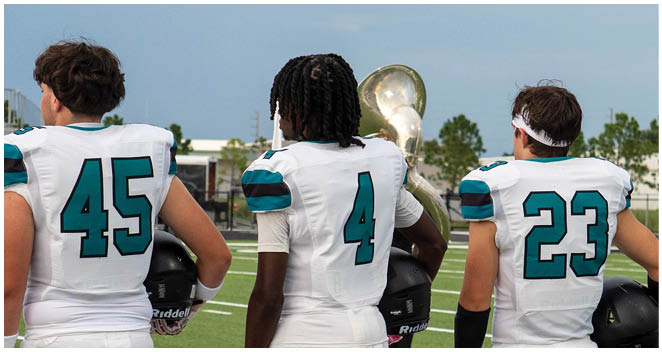 Three football players standing on a field. Description generated by AI