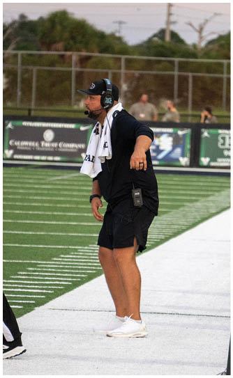 A football field with a man wearing a black shirt and white shoes. Description generated by AI