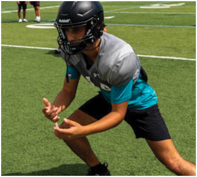 A football player in a blue and black uniform is crouching on the field. Description generated by AI
