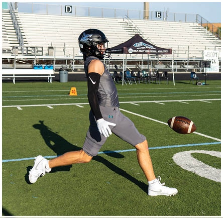 A football player in a grey shirt and shorts is throwing a football on a field. Description generated by AI
