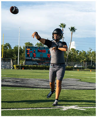 A man in a grey shirt and black helmet is throwing a football. Description generated by AI