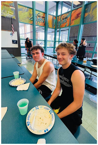 Two boys sitting at a table with plates of food in front of them. Description generated by AI