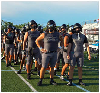 A group of people wearing grey uniforms are standing on a field. Description generated by AI