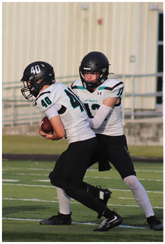 A boy in a white jersey is running with a football. Description generated by AI