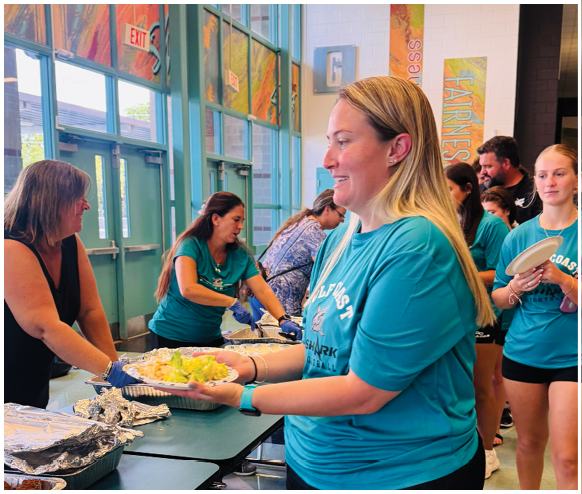 A woman wearing a blue shirt is serving food to people. Description generated by AI
