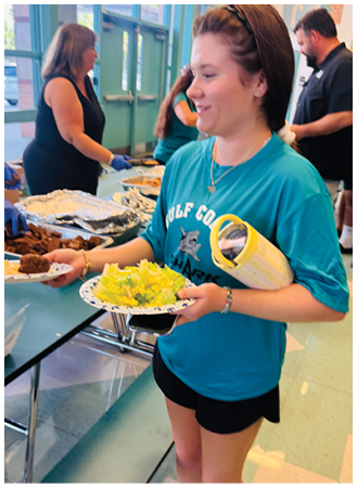 A woman wearing a blue shirt and black shorts holding a plate of salad. Description generated by AI
