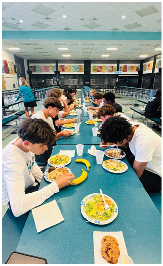 A group of people are sitting at a long table eating. Description generated by AI