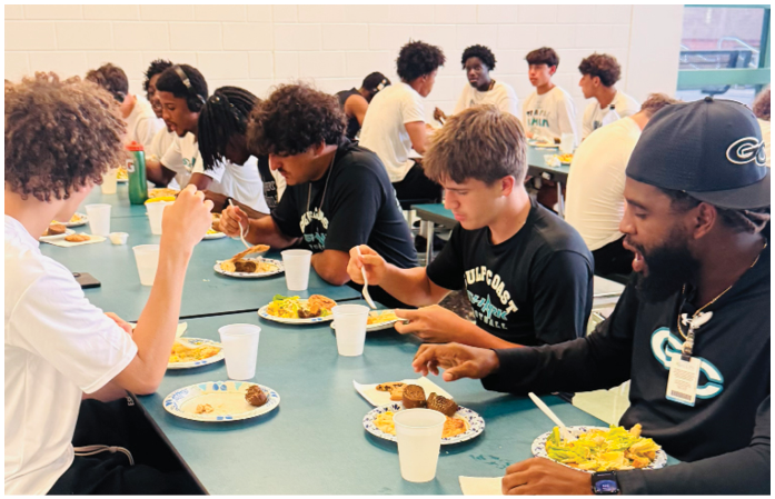 A group of people are sitting at a table eating. Description generated by AI