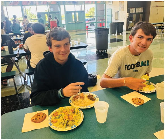 Two boys sitting at a table with plates of food. Description generated by AI