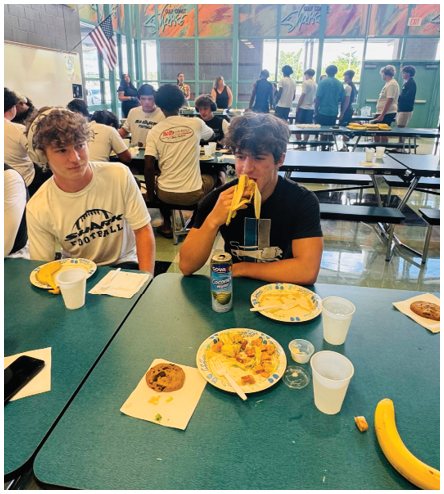 A boy eating a banana at a table. Description generated by AI