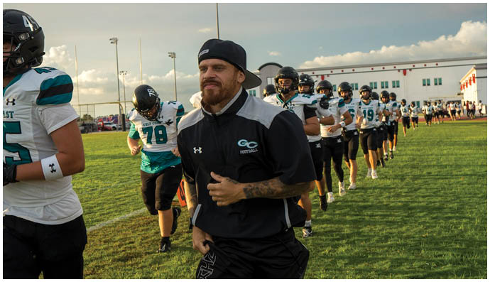 A man is running on a field with a football team behind him. Description generated by AI