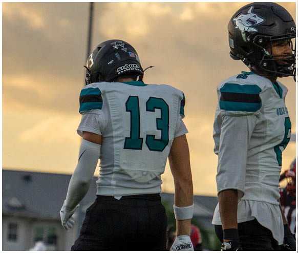 Two football players standing on a field. Description generated by AI