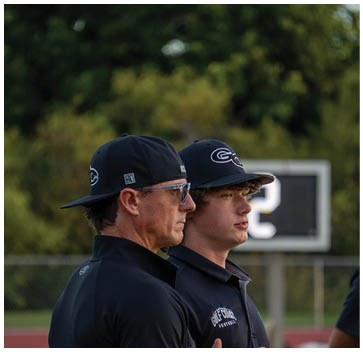 Two men wearing black shirts and hats. Description generated by AI