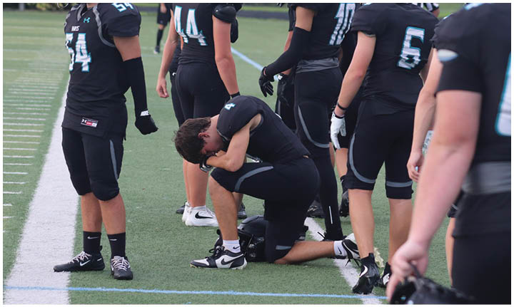 A football player kneeling on the field. Description generated by AI