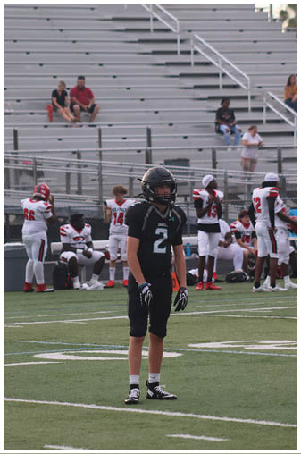 A boy wearing a football uniform stands on a field. Description generated by AI