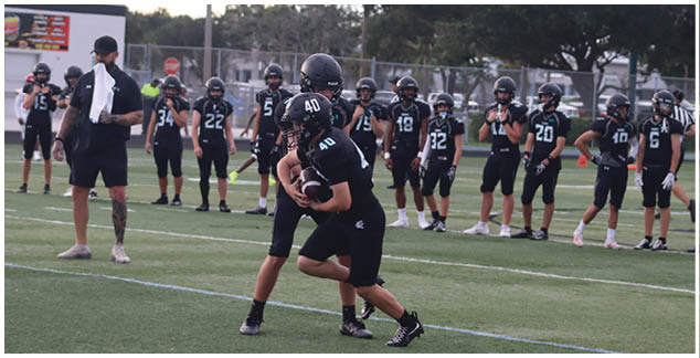 A group of young boys wearing black football uniforms are standing on a field. Description generated by AI