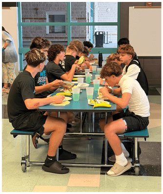 A group of young people are sitting around a table eating. Description generated by AI