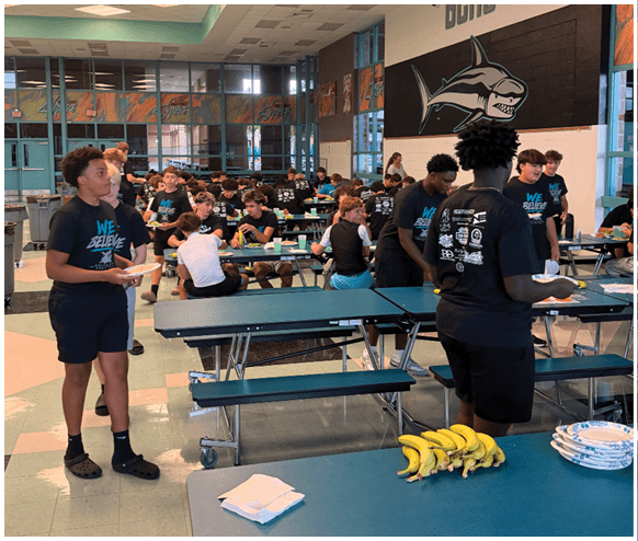 A group of people are sitting at tables in a cafeteria. Description generated by AI