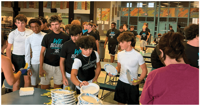 A group of people are standing around a table with plates and bowls. Description generated by AI