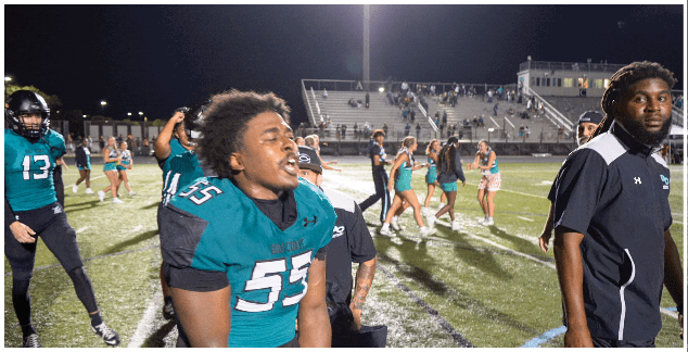 A football player wearing a green jersey with the number 53 on it. Description generated by AI