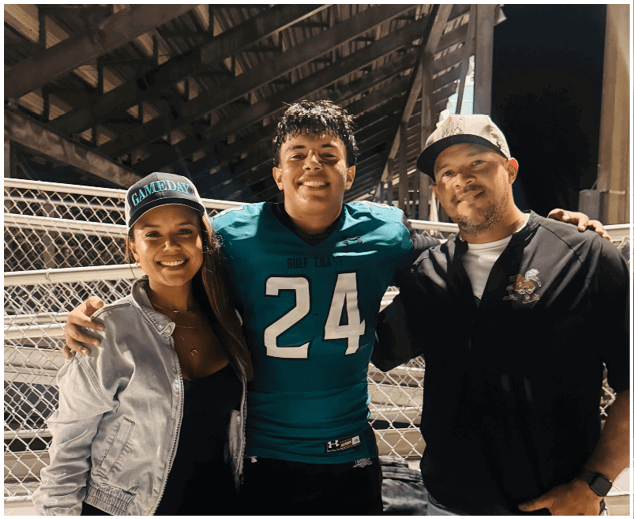 A man and a woman are standing next to a man wearing a football jersey. Description generated by AI