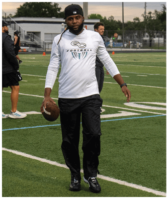 A man wearing a white shirt and black pants holding a football. Description generated by AI