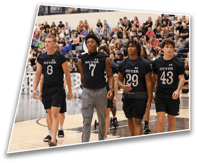 Three adults wearing black sports jerseys with numbers walk on an indoor basketball court with a crowd seated in the background. Description generated by AI