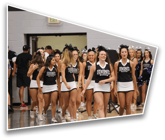 A group of people with bows in their hair are gathered indoors near a wall with an exit sign above a doorway. Description generated by AI