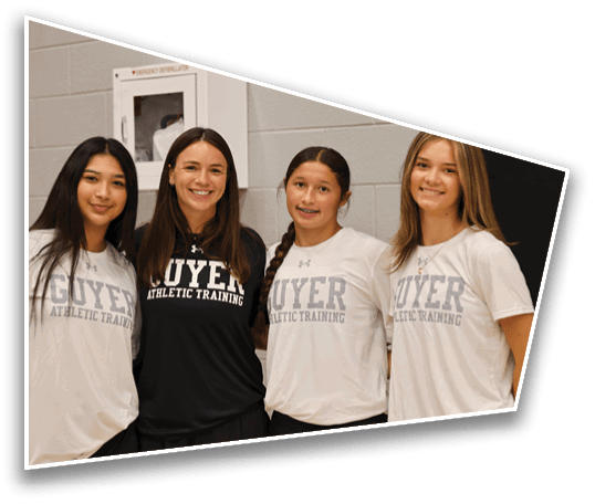 Four people wearing athletic training shirts stand closely together smiling in an indoor setting. Description generated by AI