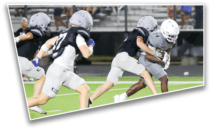 People wearing helmets and sports uniforms are playing football on a field with one person holding the ball while others attempt to tackle or chase them. Description generated by AI