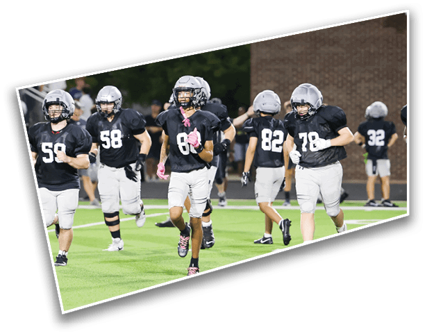 People wearing black jerseys and white pants are running on a green football field. Description generated by AI