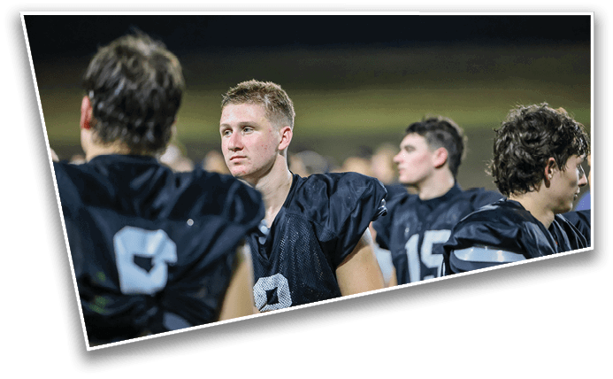 Several people wearing black football uniforms are standing together on a field at night, with one person looking directly ahead. Description generated by AI