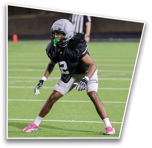 A person wearing pink cleats and athletic shorts is standing on a green sports field with legs apart in a ready stance. Description generated by AI