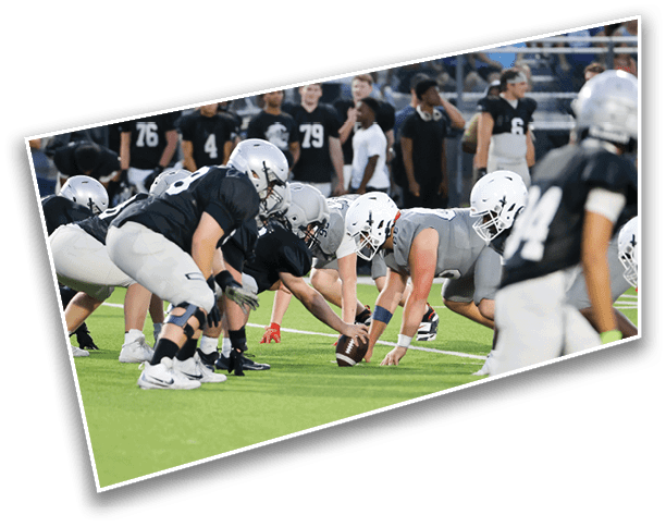 Two opposing football teams are lined up at the line of scrimmage on a green field, preparing for the next play. Description generated by AI