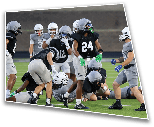 Several people wearing football helmets and uniforms are engaged in a play on a football field with some standing and others on the ground. Description generated by AI