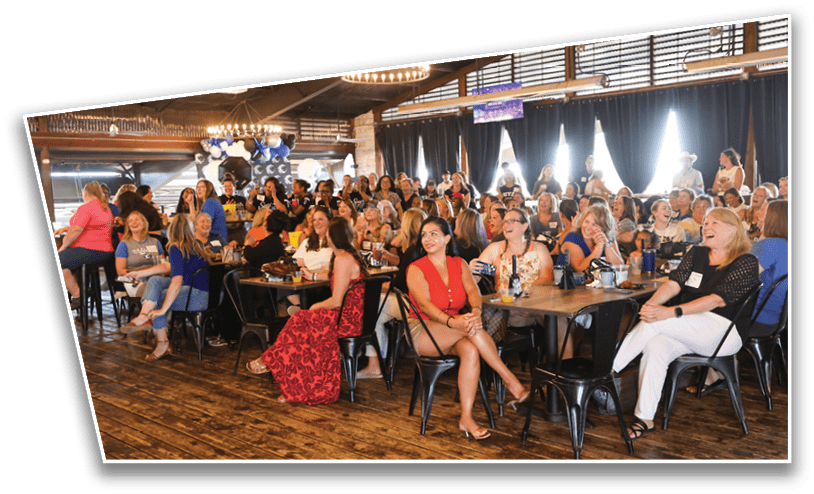 A large group of adults seated at tables in a warmly lit indoor venue appear engaged and attentive, with some smiling and clapping. Description generated by AI