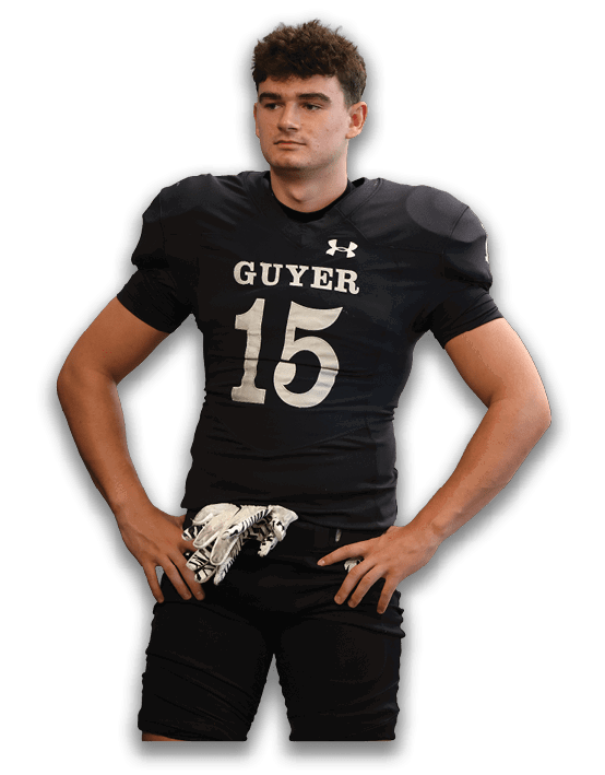 A person with short curly hair wearing a black sports jersey with an Under Armour logo is looking slightly to the side against a white background. Description generated by AI