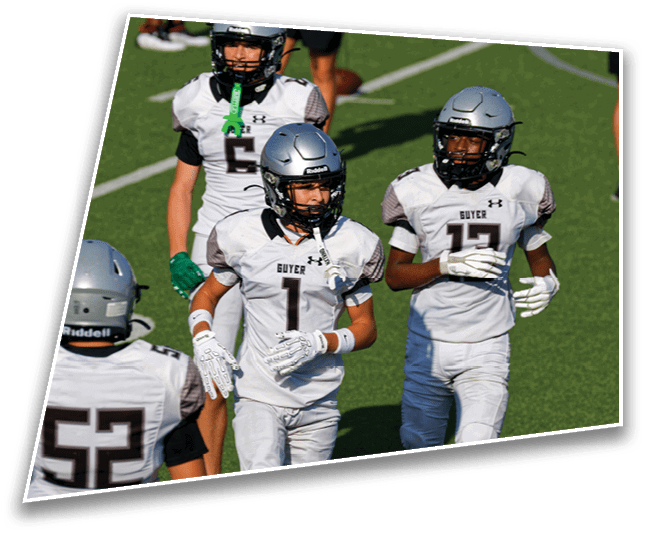 Three people wearing white football uniforms and silver helmets are walking on a green field during a game or practice. Description generated by AI