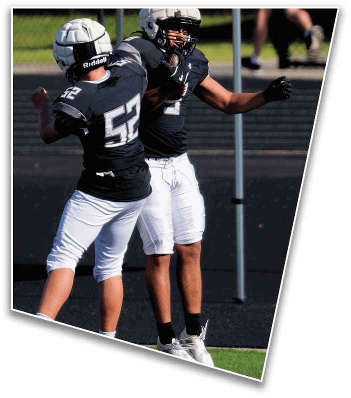 Two people wearing football helmets and uniforms are celebrating on a sports field with one person jumping and the other raising an arm. Description generated by AI