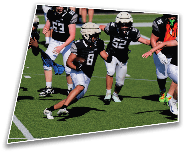 People wearing black and white football uniforms are playing on a green field with one person running while holding a football. Description generated by AI