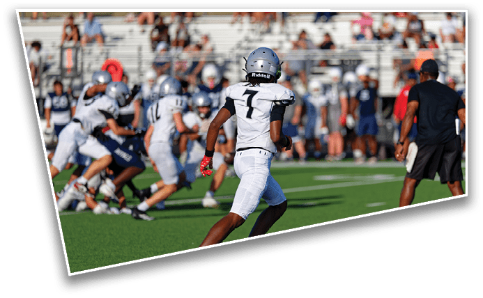 People in football uniforms are actively playing on a green field with a crowd in the background. Description generated by AI