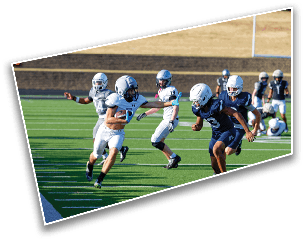 People wearing helmets and football uniforms are actively playing a game on a green field with yard lines. Description generated by AI