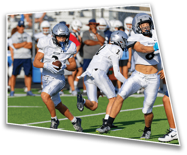 People in white football uniforms are playing on a green field with one person holding the ball and others running nearby. Description generated by AI