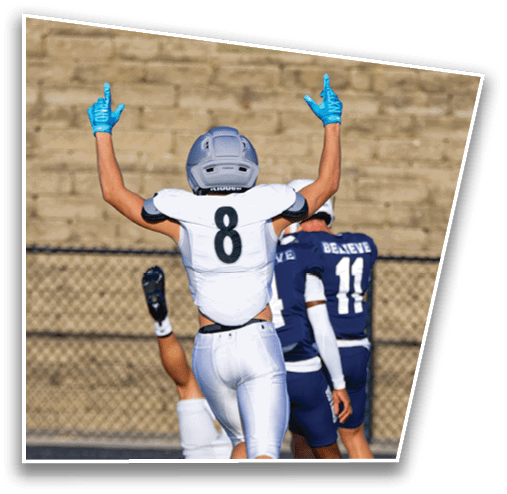A person wearing a white sports jersey with the number eight and blue gloves raises both arms with index fingers pointing upward on a sports field. Description generated by AI
