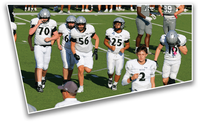 A group of people wearing white football uniforms and helmets are running on a green field during a game or practice. Description generated by AI