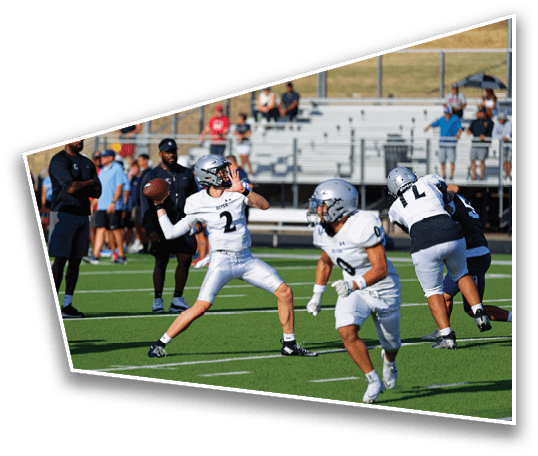 People in sports uniforms are playing football on a field while others in casual clothing watch from the sidelines and bleachers. Description generated by AI